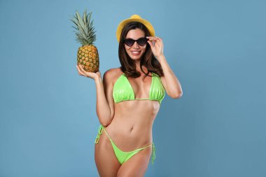 Mavi arka planda ananas olan şık bikinili güzel bir kadın.