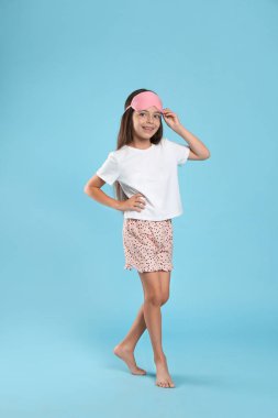 Açık mavi arka planda pijama ve uyku maskesi giyen tatlı bir kız.