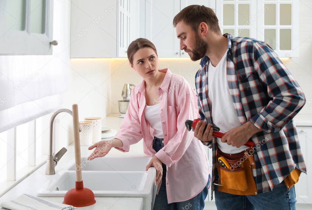 Young woman complaining to plumber about clogged sink in kitchen