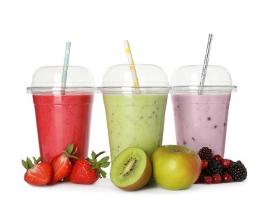 Plastik bardaklarda pipetli farklı meyve suları ve beyaz arka planda taze meyveler