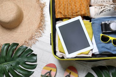 Tablet ve seyahat aksesuarlarıyla dolu bir bavul. Yaz tatili