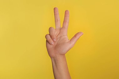 Genç çocuk sarı arka planda üç parmak gösteriyor, yakın plan.