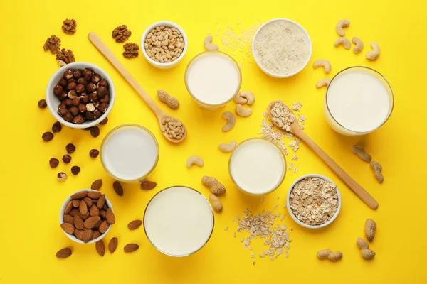 Different vegan milks and ingredients on yellow background, flat lay