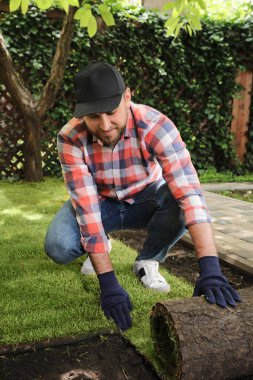 Genç adam çimenleri arka bahçeye seriyor.