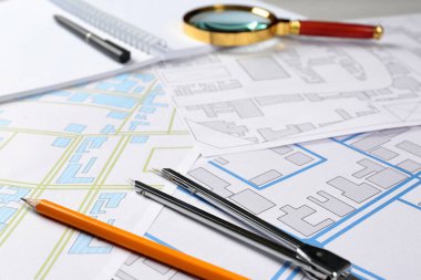 Office stationery and cadastral maps of territory with buildings on table clipart