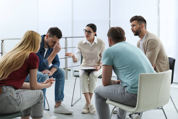 Psychotherapist working with group of drug addicted people at therapy session indoors