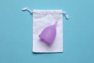 Açık mavi arka planda pamuk torbalı aybaşı bardağı, üst manzara. Yeniden kullanılabilir kadın hijyen ürünü