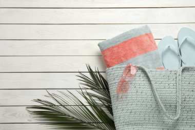 Havlulu plaj çantası, terlikler ve beyaz ahşap arka planda güneş gözlüğü, düz yatış. Metin için boşluk