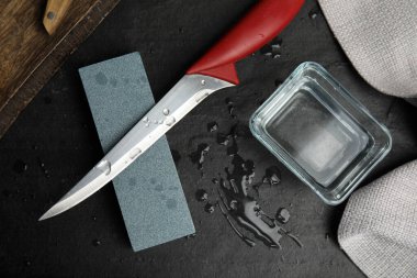 Sharpening stone, knife and water on black table, flat lay clipart
