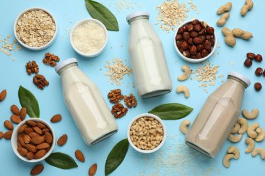 Different vegan milks and ingredients on light blue background, flat lay clipart