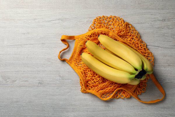 Net bag with bananas on white wooden table, top view. Space for text