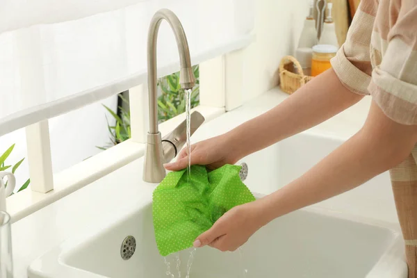 Woman washing beeswax food wrap under tap water in kitchen sink, closeup