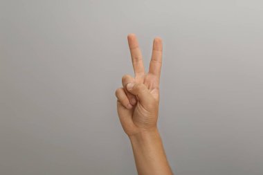 Genç çocuk açık gri arka planda iki parmağını gösteriyor, yakın plan.