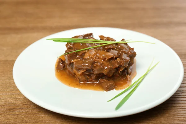 Plate with wet pet food and grass on wooden table