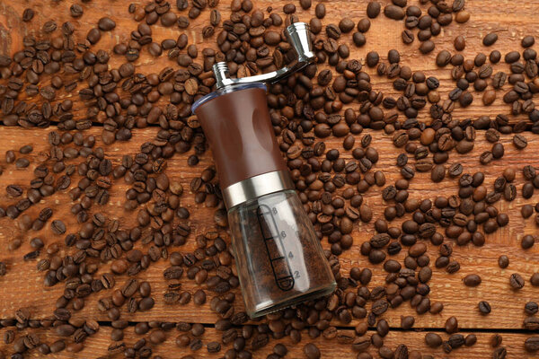 Modern manual coffee grinder with beans on wooden table, flat lay