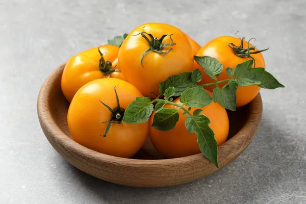 Fresh ripe yellow tomatoes with leaves on light grey table