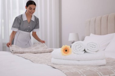 Oda hizmetçisi otel odasında yatak yapıyor, temiz havlulara odaklan. Metin için boşluk