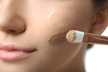 Girl applying foundation and concealer with brush on white background, closeup. Face contouring clipart