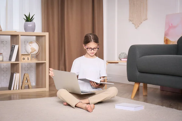 ノートパソコンと本が床に家に座っている女の子 — ストック写真