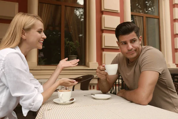 Man having boring date with talkative woman in outdoor cafe