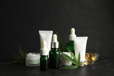 Siyah taş masa üzerinde CBD yağı, THC tentür ve kenevir yaprakları bileşimi