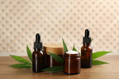 Krema, kenevir yaprağı, CBD yağı şişeleri ve ahşap masada THC tentürü.