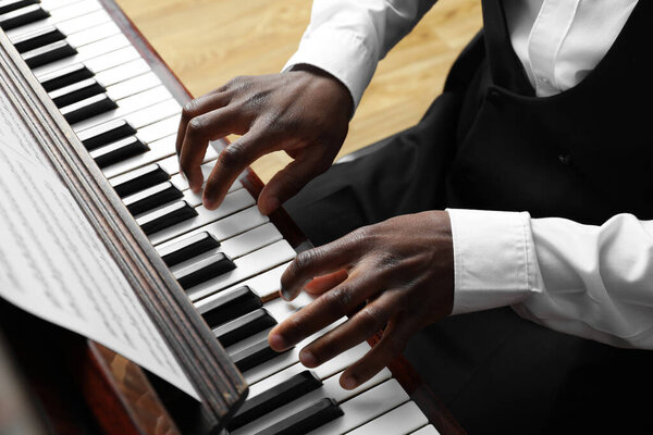 African-American man playing piano indoors, closeup. Talented musician