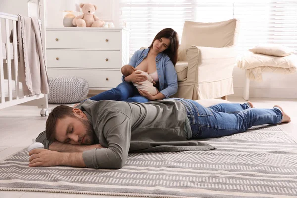 Tired young parents with their baby sleeping on floor in children\'s room