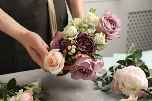 Florist creating beautiful bouquet at light grey table indoors, closeup