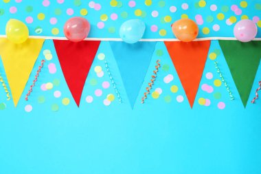Renkli üçgen bayraklar, balonlar, flamalar ve açık mavi arka planda konfeti, düz bir zemin. Metin için boşluk