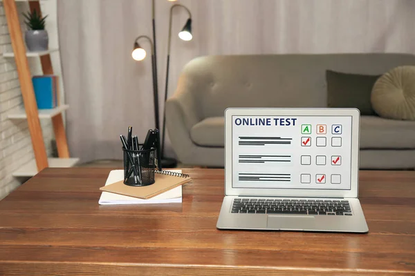 Laptop with online test and stationery on table at home