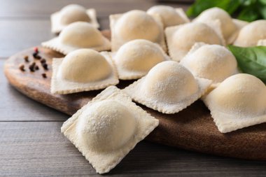 Pişmemiş ravioli, fesleğen ve biberler ahşap masada, yakın plan.