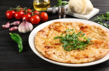 Peynirli, roka ve sebzeli lezzetli khachapuri. Koyu ahşap masa, yakın plan.