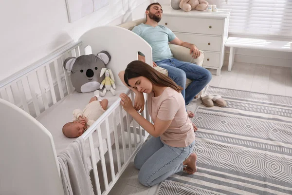 Tired young parents and their baby sleeping in children\'s room