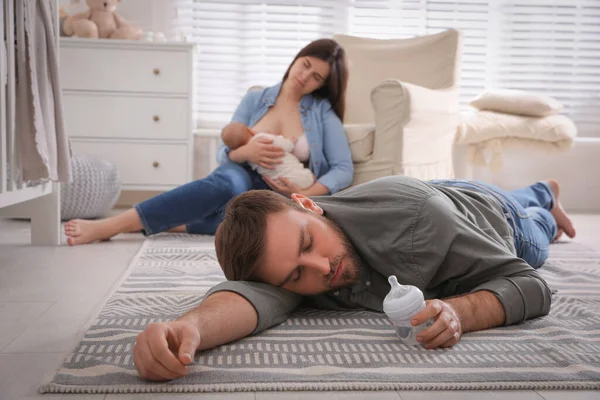 Tired young parents with their baby sleeping on floor in children\'s room
