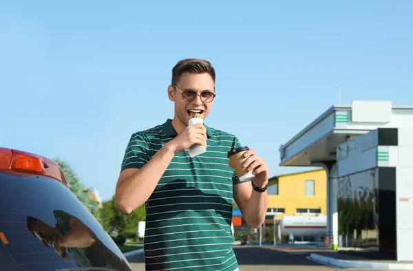 Jongeman Met Koffie Etende Hotdog Buurt Van Auto Bij Tankstation — Stockfoto