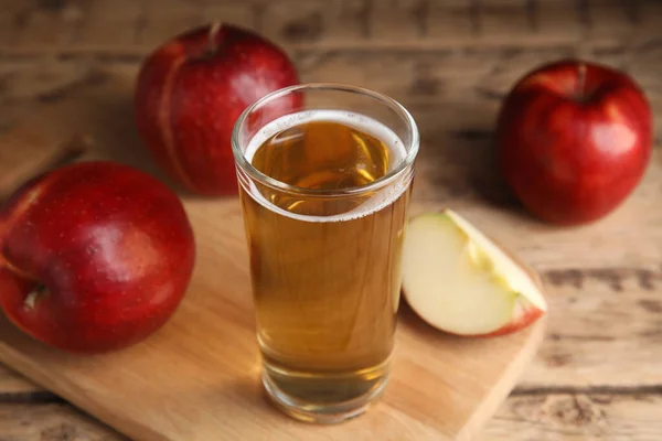 Glass of delicious cider and ripe red apples on wooden table