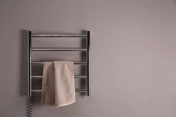 Modern heated towel rail with warm soft towel on grey wall. Space for text
