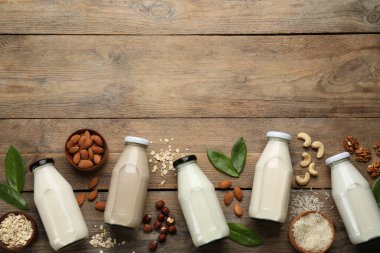 Different vegan milks and ingredients on wooden table, flat lay. Space for text clipart