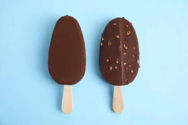 Ice cream bars glazed in chocolate on light blue background, flat lay