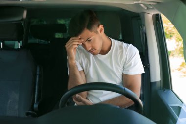 Stresli adam modern arabanın sürücü koltuğunda, ön camdan bakıyor.