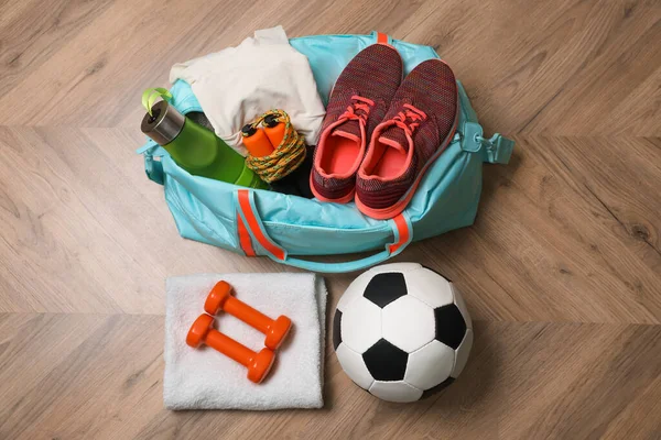 Blue gym bag and sports accessories on wooden floor, flat lay