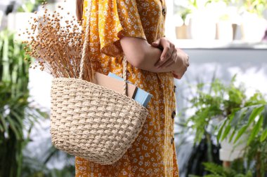 Kitaplarla dolu bir kumsal çantası ve güzel bir buket kurumuş çiçek tutan kadın, yakın plan.