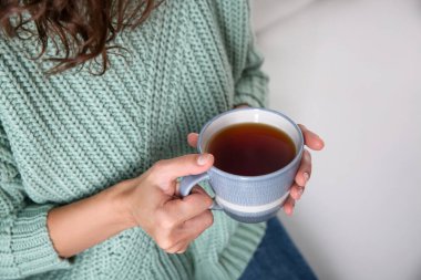 Kapalı mekanda bir fincan sıcak çay içen kadın, yakın plan. Sıcak ev atmosferi