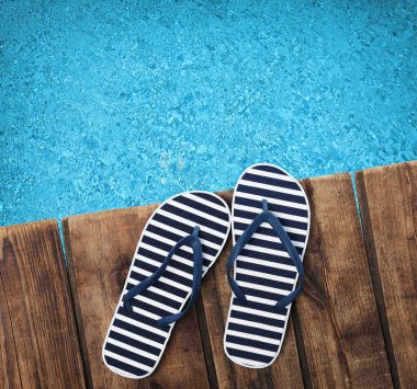 Yüzme havuzunun yanındaki ahşap güvertede bir çift parmak arası terlik.  