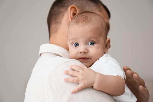 Father holding his cute baby on grey background