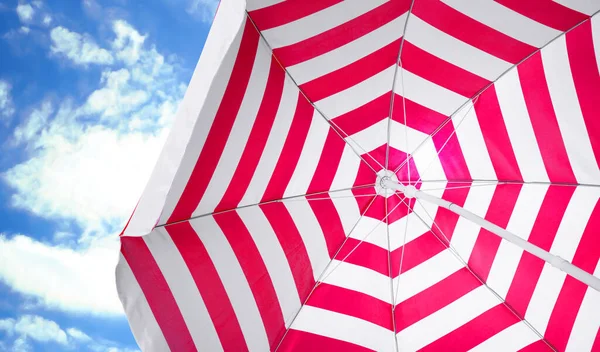 Open big striped beach umbrella and beautiful blue sky with white clouds on background