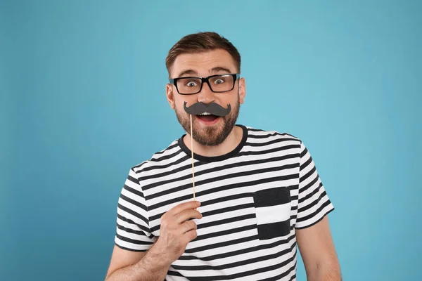 Emotional man with fake mustache on turquoise background