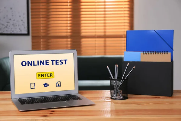 Laptop with online test and stationery on table in office