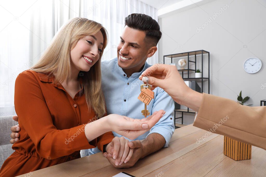 Real estate agent giving house key to couple at table in office